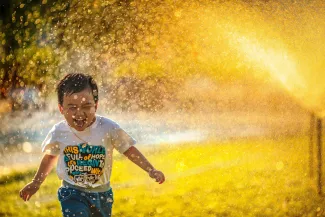 a young boy running through a sprinkle of water by MI PHAM courtesy of Unsplash.