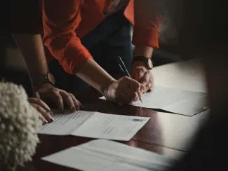 person in orange long sleeve shirt writing on white paper by Romain Dancre courtesy of Unsplash.