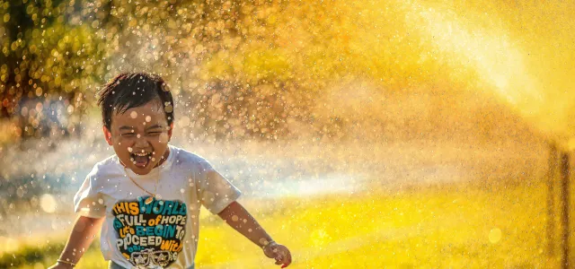 a young boy running through a sprinkle of water by MI PHAM courtesy of Unsplash.