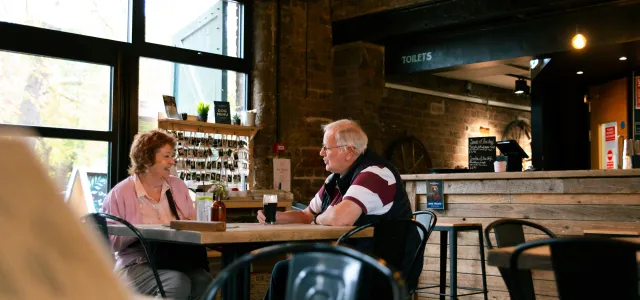 Elderly couple talking at a cafe table by Centre for Ageing Better courtesy of Unsplash.